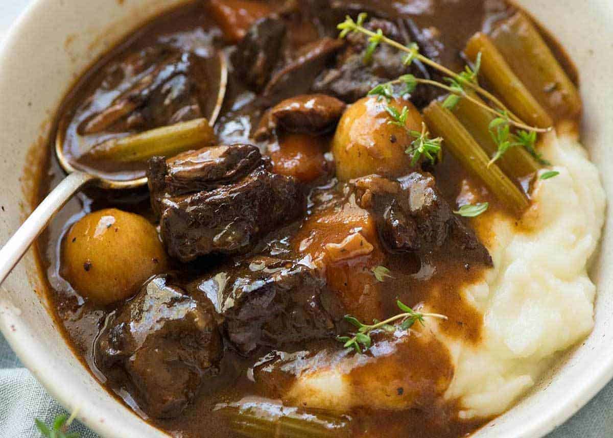 Photo of Beef Stew over mashed potato in a rustic cream bowl.