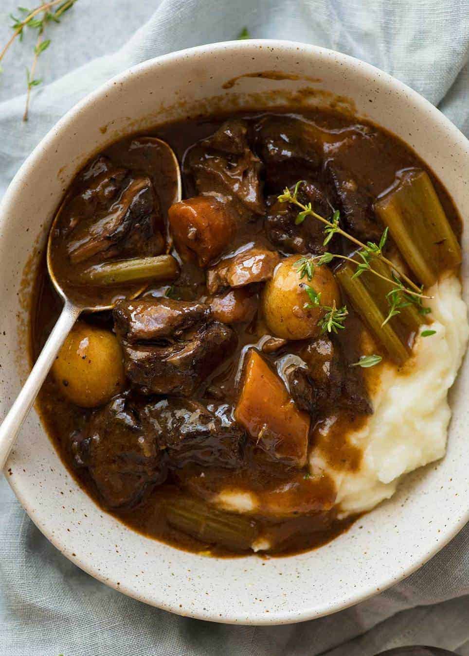 Overhead photo of Beef Stew over mashed potato in a rustic cream bowl.