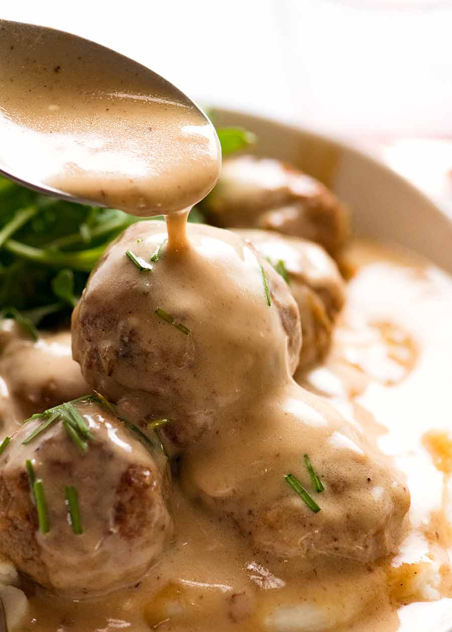 Spoon drizzling sauce over Swedish Meatballs